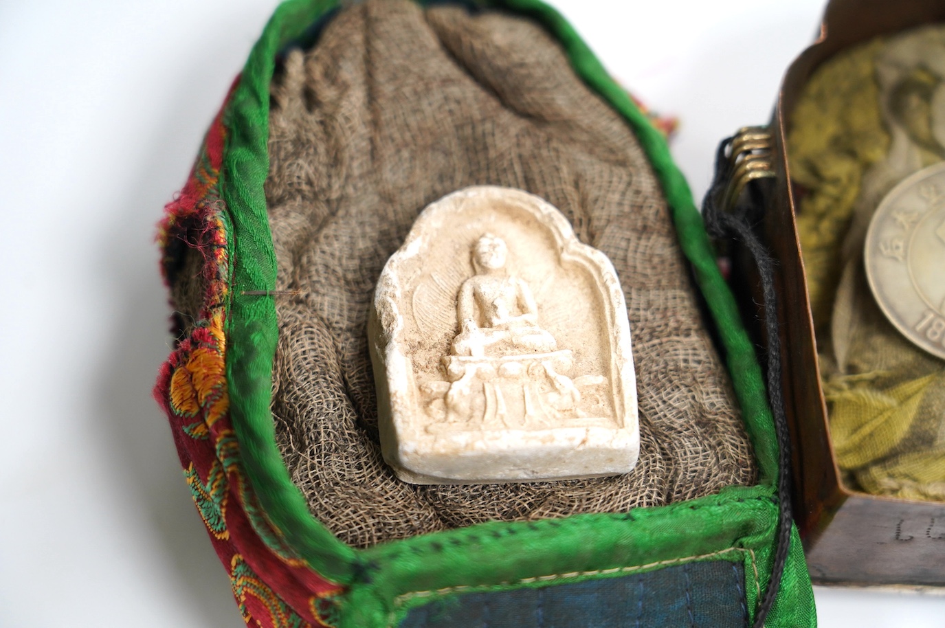 A Tibetan repoussé white metal and copper travelling shrine in a quilted cloth case, 10.5cm high. Condition - fair